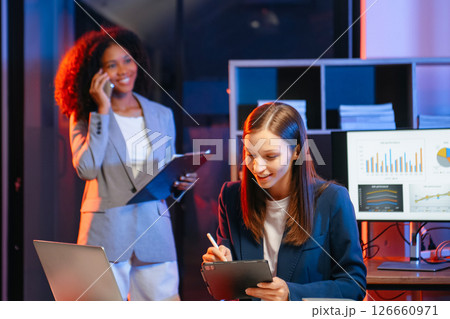 Two business workers talking on the smartphone and using laptop at the office. overtime Two business workers talking on the smartphone and using laptop at the office. overtime 126660971