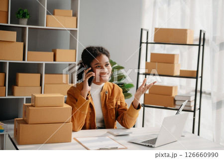 Young African woman prepare parcel box and standing check online orders for deliver to customer on tablet, laptop Shopping Online concept. Young African woman prepare parcel box and standing check online orders for deliver to customer on tablet, laptop Shopping Online concept. 126660990