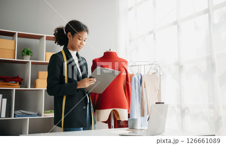 Diverse female fashion designers at work with tailor centimeters on necks and holds tablet and smartphone. independent creative design business. Diverse female fashion designers at work with tailor centimeters on necks and holds tablet and smartphone. independent creative design business. 126661089