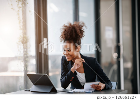Beautiful Asian woman using laptop and tablet while sitting at her working place. Concentrated at work. Beautiful Asian woman using laptop and tablet while sitting at her working place. Concentrated at work. 126661227