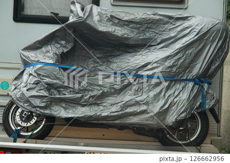 Motorcycle is covered with a grey plastic tarp Motorcycle is covered with a grey plastic tarp 126662956