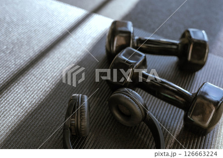 Black dumbbells for sports and acoustic headphones lie on the floor in the gym on a stylish yoga mat 126663224