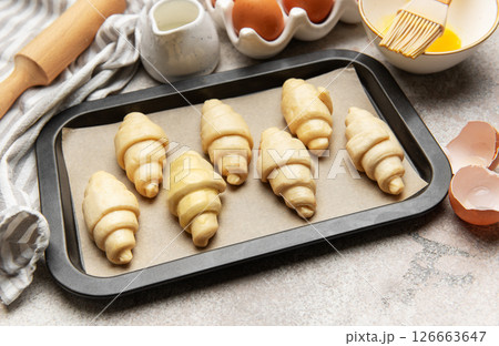 Baking tray with raw croissants, waiting to be cooked, surrounded by kitchen utensils 126663647