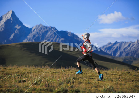 Fitness woman trail runner running in grassland with snow capped mountains in the background 126663947