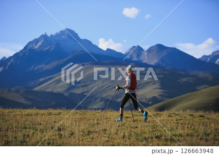Fitness woman trail runner running in grassland with snow capped mountains in the background Fitness woman trail runner running in grassland with snow capped mountains in the background 126663948