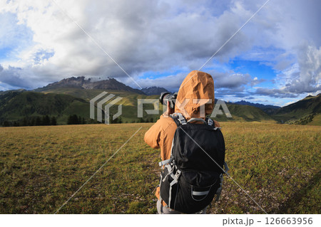 Woman backpacker hiking on high altitude mountains taking picture of the snow capped mountain in the distance Woman backpacker hiking on high altitude mountains taking picture of the snow capped mountain in the distance 126663956