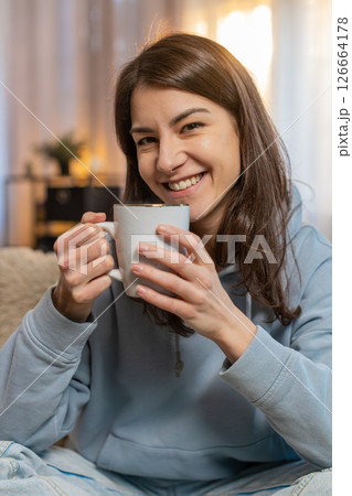 Happy young woman smelling drinking cup of hot coffee, taking a break, relaxing on sofa at home 126664178