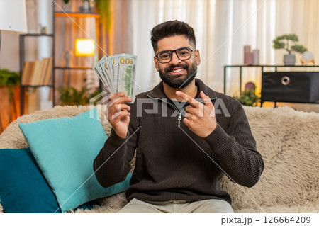 Indian man happily counting cash money on sofa at home, celebrating income or lottery jackpot Indian man happily counting cash money on sofa at home, celebrating income or lottery jackpot 126664209