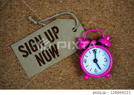 Sign Up Now text on price tag with alarm clock on cork board background Sign Up Now text on price tag with alarm clock on cork board background 126664223