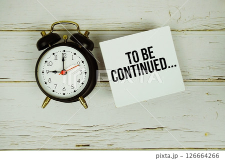 To be continued... text message on sticky note with alarm clock on wooden background To be continued... text message on sticky note with alarm clock on wooden background 126664266