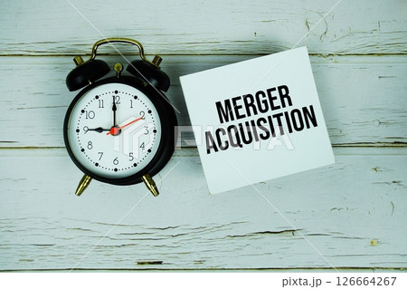 Merger Acquisition text message on sticky note with alarm clock on wooden background Merger Acquisition text message on sticky note with alarm clock on wooden background 126664267