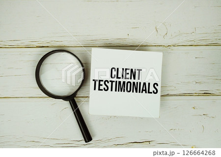 Client Testimonials text message on sticky note with magnifying glass on wooden background 126664268