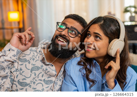 Indian couple man woman dancing together to music in headphones at home, sharing joyful rhythmic hug Indian couple man woman dancing together to music in headphones at home, sharing joyful rhythmic hug 126664315
