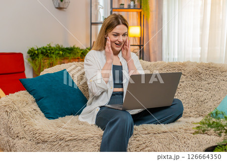 Woman surprised by good news on laptop at home, wow expression excitement, amazed, celebrate win 126664350
