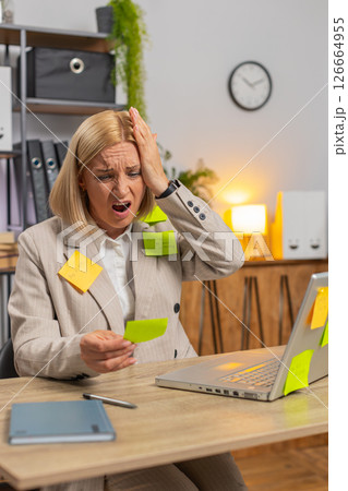 Exhausted Caucasian mature businesswoman with sticky notes and laptop sitting at home office desk 126664955