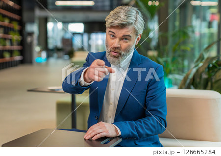 Portrait of Caucasian mature businessman pointing to camera choosing hire sitting in office lobby Portrait of Caucasian mature businessman pointing to camera choosing hire sitting in office lobby 126665284