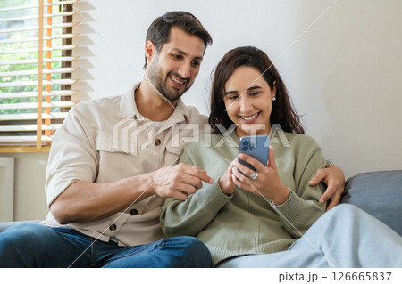 Hispanic Couple sharing social media moments together at home, enjoying digital connection and lifestyle interaction through smartphone Hispanic Couple sharing social media moments together at home, enjoying digital connection and lifestyle interaction through smartphone 126665837