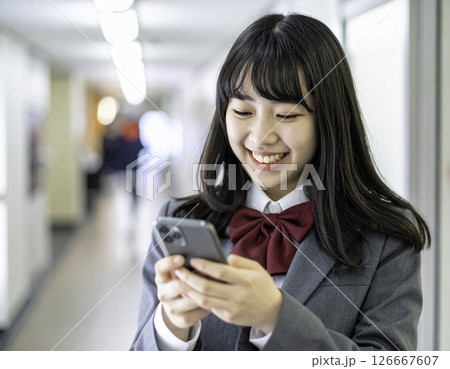スマホで笑顔になる女子高校生｜登校中の校舎での一コマ 126667607