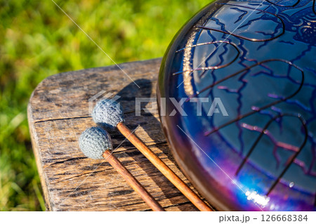 Steel tongue drum and mallets resting on a wooden bench. Concept of sacred stillness, sound meditation, and harmony with nature Steel tongue drum and mallets resting on a wooden bench. Concept of sacred stillness, sound meditation, and harmony with nature 126668384