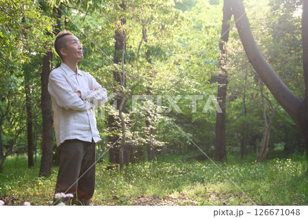 雑木林の中で太陽の光を受けて輝く若葉と佇む男性 雑木林の中で太陽の光を受けて輝く若葉と佇む男性 126671048