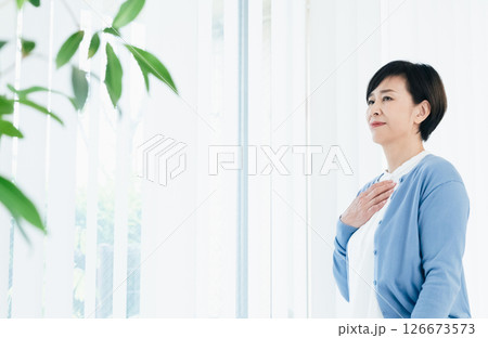 窓際で胸に手を当てる中高年女性 126673573