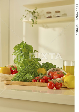 Tomatoes, lemons, and leafy greens arranged in a neat composition on a clean kitchen island in a minimal, well-lit kitchen space. Mesh bag full of food on table in modern kitchen interior Tomatoes, lemons, and leafy greens arranged in a neat composition on a clean kitchen island in a minimal, well-lit kitchen space. Mesh bag full of food on table in modern kitchen interior 126674344