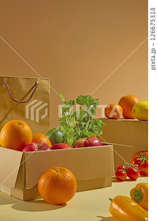 Front view of cartons and paper bags filled with fresh fruits and vegetables on brown background. Colorful vegetable such as tomatoes, orange, bell pepper, apple and celery 126675318