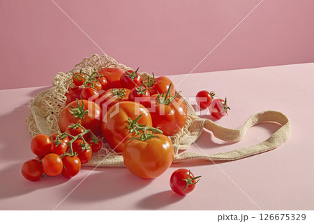 A side-view image of fresh vegetables, including cherry tomatoes, spilling out of a mesh bag onto a pastel pink surface. Gentle shadows and highlights create a soft, natural feel with ample copy space A side-view image of fresh vegetables, including cherry tomatoes, spilling out of a mesh bag onto a pastel pink surface. Gentle shadows and highlights create a soft, natural feel with ample copy space 126675329
