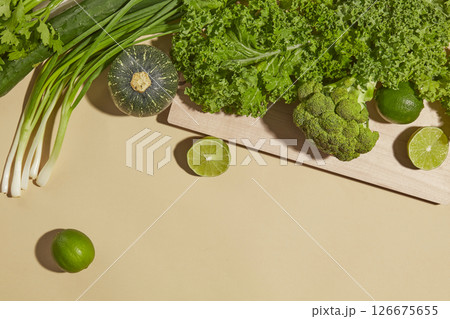 Top view of fresh green onions, leafy greens, and limes arranged with herbs on a tan surface. The raw textures highlight freshness in natural food styling photography. 126675655