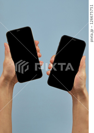 woman holding two smartphones with blank screens on blue background 126675751