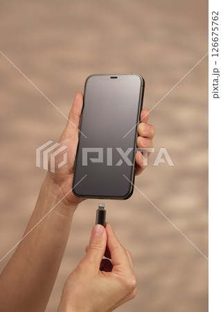 female hand plugging charger cord into smartphone to charge battery on beige background, Wired charging 126675762