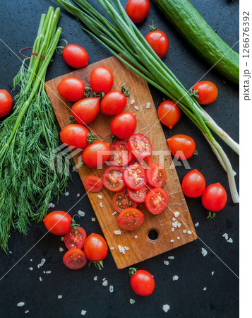 Fresh red cherry tomatoes with herbs and leek sprinkled with sea salt on the wooden board on the table, top view of vegetables covered with drops. Fresh red cherry tomatoes with herbs and leek sprinkled with sea salt on the wooden board on the table, top view of vegetables covered with drops. 126676392