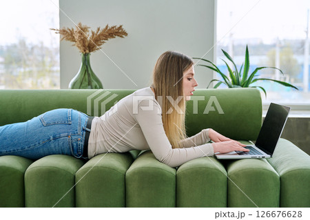 Young woman lying on sofa at home using laptop Young woman lying on sofa at home using laptop 126676628