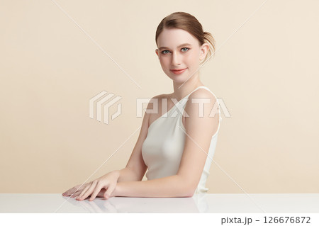 A beautiful young woman with clean, fresh skin against a beige background. Skincare, facial treatment, cosmetology, beauty, and spa. An elegant portrait of an woman. 126676872