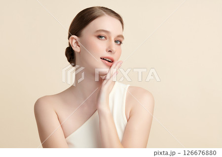 A beautiful young woman with clean, fresh skin against a beige background. Skincare, facial treatment, cosmetology, beauty, and spa. An elegant portrait of an woman. 126676880