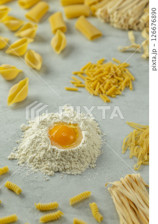 Variety of uncooked pasta with flour and egg yolk forming a circle on a gray background 126676890