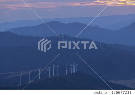 Wind turbines generating clean energy during a colorful sunset over mountains 126677231
