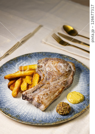 Grilled pork chop served with french fries and mustard on elegant blue plate 126677317