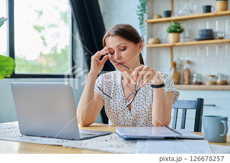 Middle aged sad stressed woman sitting at home at table with computer Middle aged sad stressed woman sitting at home at table with computer 126678257