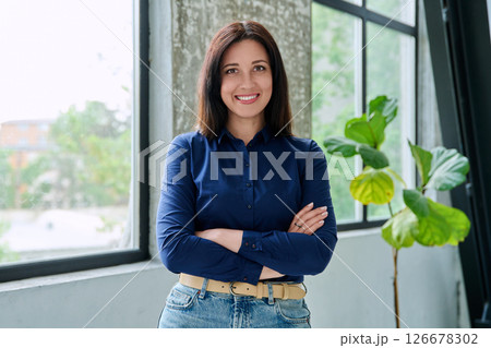 Portrait of beautiful confident brunette woman looking at camera with crossed arms, near window Portrait of beautiful confident brunette woman looking at camera with crossed arms, near window 126678302