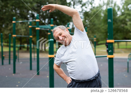 Elderly man doing gymnastics on an outdoor sports ground 126678568