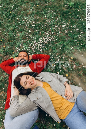 Two people,woman and man relaxing together on grassy field with small white wildflowers in summer, enjoying peaceful moment outdoors.Casual clothing and natural surroundings create a calm, authentic, Two people,woman and man relaxing together on grassy field with small white wildflowers in summer, enjoying peaceful moment outdoors.Casual clothing and natural surroundings create a calm, authentic, 126679968