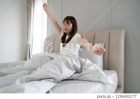Happy woman morning stretching and wake up in home bedroom after sleeping or rest. Relax, peace and comfort of Asian woman smiling with wellness and feeling fresh, awake and well rested in house. 126680277