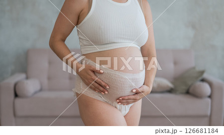 Caucasian pregnant woman in adult diapers suffers from incontinence. Close-up of belly.  126681184