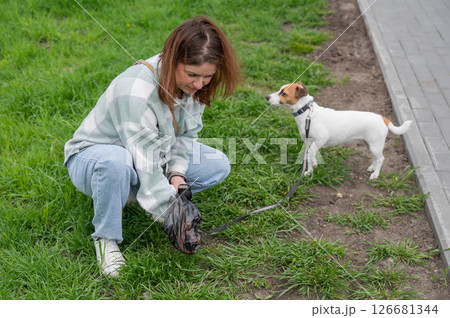 A woman cleans up dog excrement while on a walk. A woman cleans up dog excrement while on a walk. 126681344