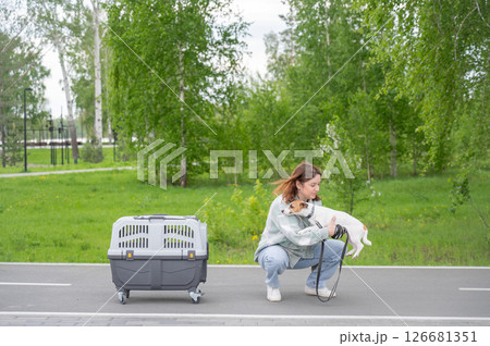 Owner walks Jack Russell Terrier and carries cage for safe travel. 126681351