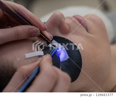 A woman undergoing eyelash extension procedure using an ultraviolet lamp. A woman undergoing eyelash extension procedure using an ultraviolet lamp. 126681377