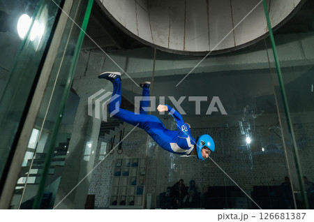 A man in overalls and a protective helmet enjoys flying in a wind tunnel. Free fall simulator 126681387