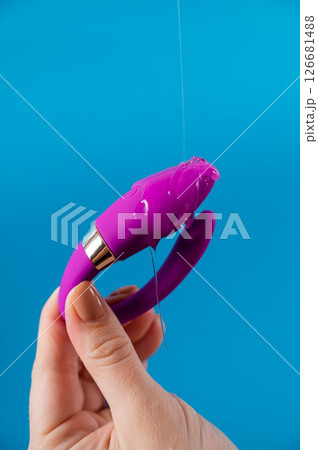 A woman holds a curved sex toy in lubrication on a blue background. Vaginally clitoral vibrator. A woman holds a curved sex toy in lubrication on a blue background. Vaginally clitoral vibrator. 126681488
