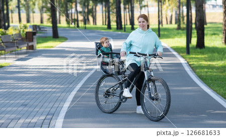 Caucasian woman riding a bicycle with her toddler son sitting behind her in a child seat. Caucasian woman riding a bicycle with her toddler son sitting behind her in a child seat. 126681633